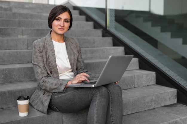 Side view of businesswoman having coffee and working on laptop on steps