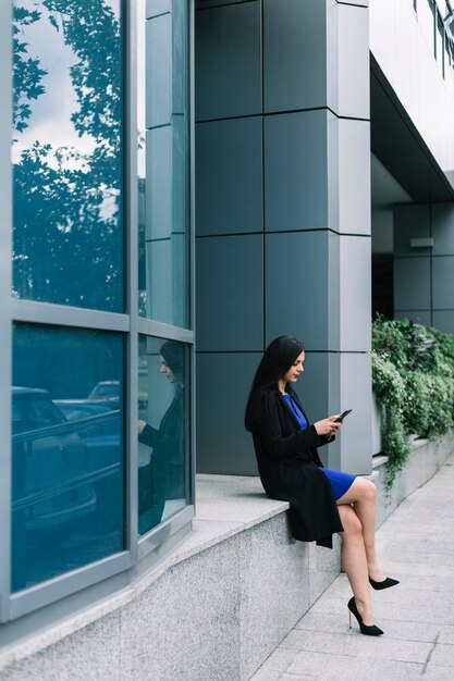 Side view of a businesswoman using smartphone outside office building