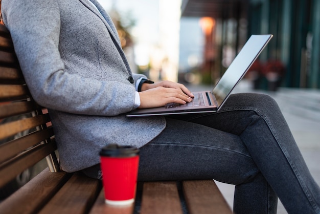 Free photo side view of businesswoman working on laptop outdoors with cup of coffee