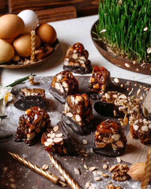 Side view of candy with caramel dark chocolate and roasted hazelnuts on a wooden board