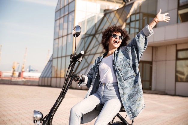 Side view of carefree woman in sunglasses sitting on motorbike