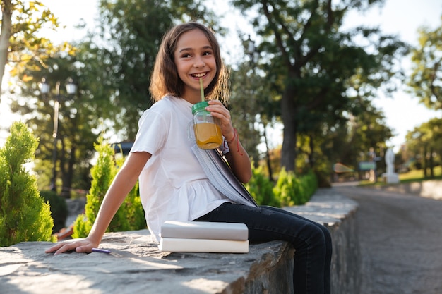 Side view of cheerful young brunette girl sitting outdoors