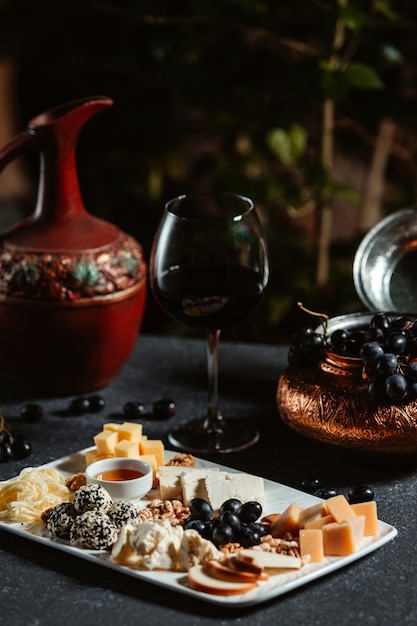 Side view of cheese plate served with grape and honey on black table