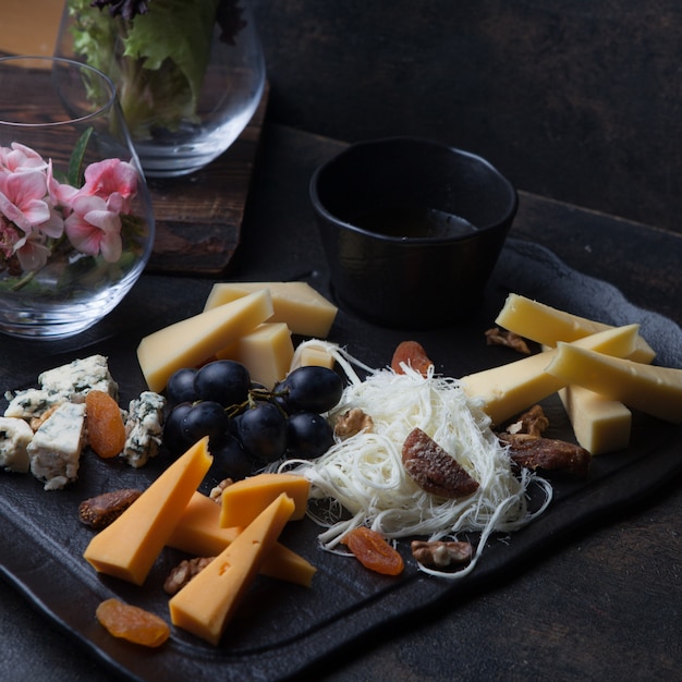 Free photo side view cheese platter with grapes and nuts and honey in tray