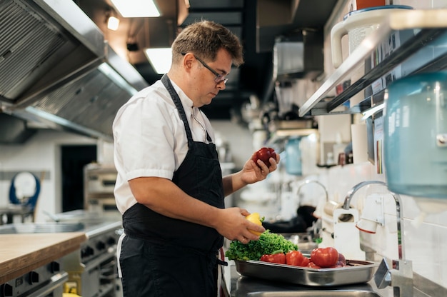 Free Photo side view of chef with apron checking vegetables in the kitchen