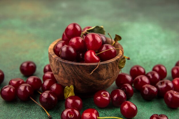 Side view of cherries in wooden bowl and on green background