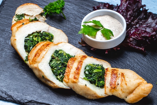 Free photo side view chicken breast stuffed with spinach and sauce on the table