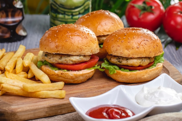 Side view chicken burgers with french fries ketchup and mayonnaise on the board