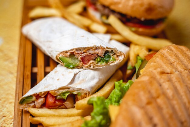 Side view chicken doner with tomato sauce cucumber in pita and french fries on the table