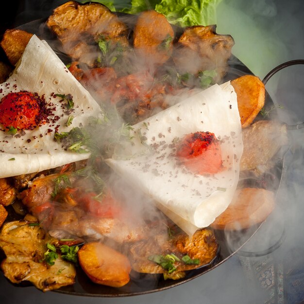 Side view chicken sac with fried potatoes and tomato and lavash in smoke