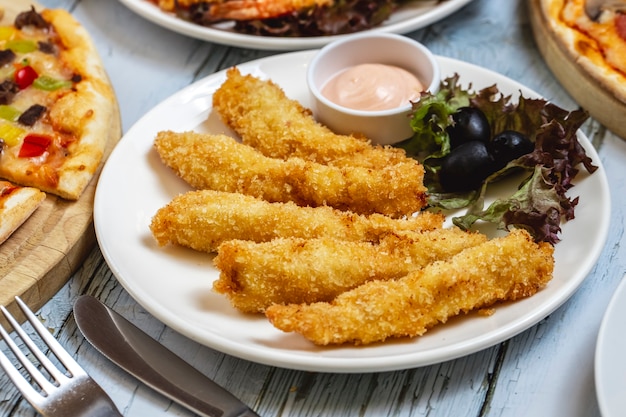 Side view chicken strips with black olive lettuce and sauce on a plate