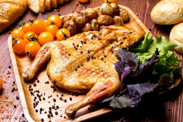 Side view chicken tobacco with potatoes and yellow cherry tomatoes with basil on a tray