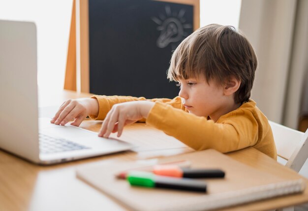 Side view of child at desk with laptop and blackboard