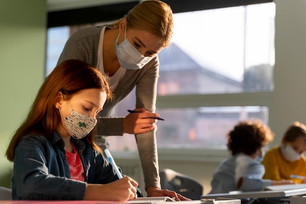 Free photo side view of children learning in school with teacher during the pandemic