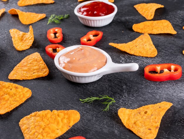 Side view chips pattern with pepper dill and sauses in bowls on black stone horizontal