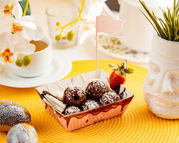 Side view of chocolate balls with coconut sprinkles and strawberry in a cardboard bag