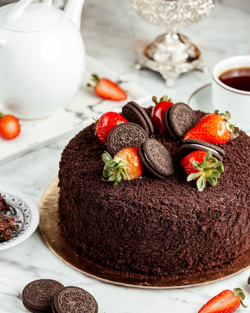 Side view of chocolate cake decorated with strawberries and cookies on the table