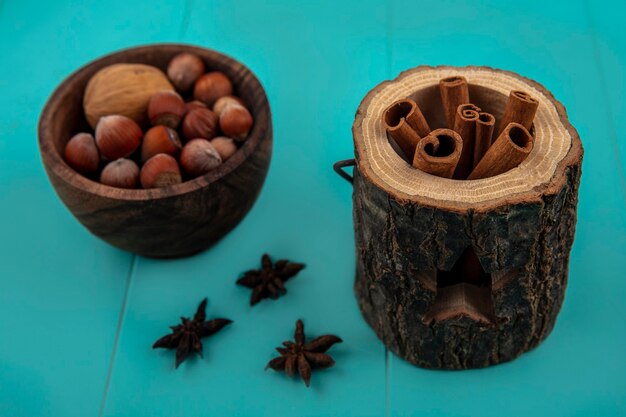 Side view of cinnamon in tree bowl and bowl of nuts on blue background