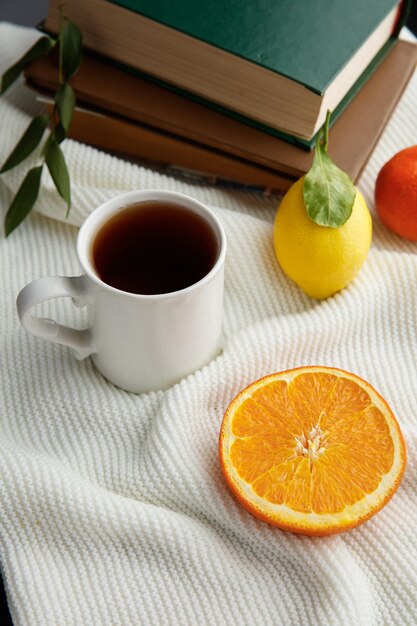 Side view of citrus fruits as orange slice and lemon tangerine with cup of tea and closed books on white background