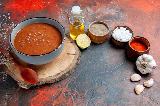 Free photo side view of classic tomato soup on wooden tray different spices and oil bottle lemon garlic on mixed color table