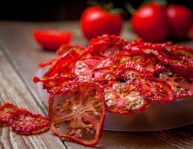 Side view close-up dried tomatoes in plate and fresh tomatoes on wooden table