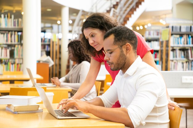 Side view of colleagues working with laptop at library