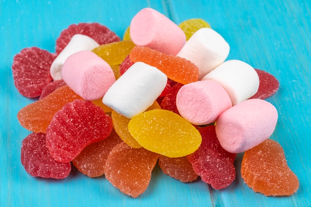 Side view of colorful tasty marmalade candies and marshmallows scattered on blue