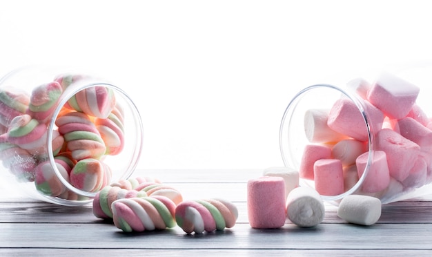 Free photo side view of colorful twisted marshmallow scattered from a glass jar on white