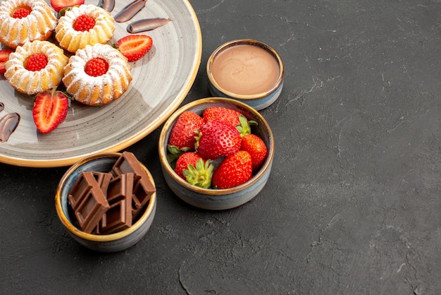 Side view cookies and strawberries appetizing cookies with strawberries on plate next to bowls of strawberries chocolate and chocolate cream on table