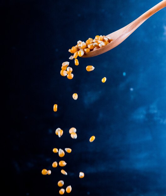 Side view of corn seeds falling from a wooden spoon