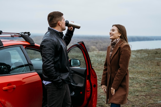 Free photo side view of couple next to car drinking from thermos