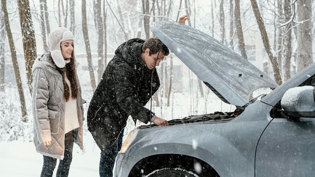 Side view of couple checking car engine while on a road trip