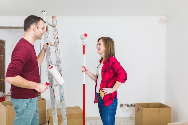 Free Photo side view couple with paint rollers and ladder