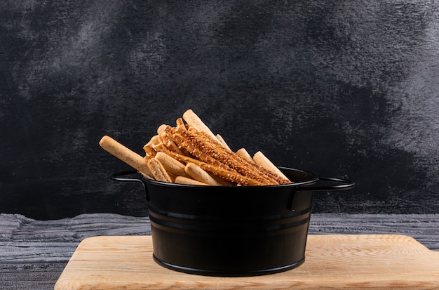 Free Photo side view of crackers in black pan and wooden cutting board on dark  horizontal