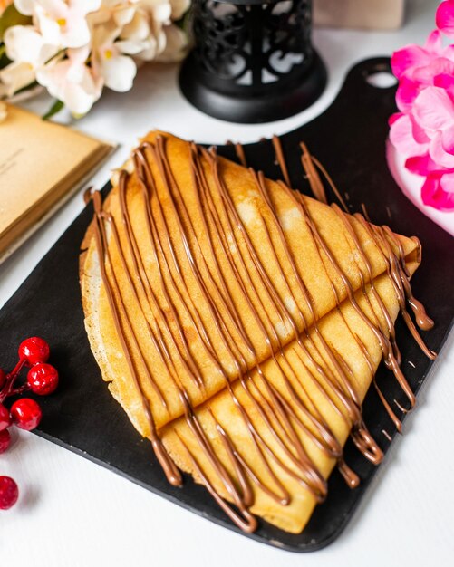 Side view of crepe with chocolate cocoa syrup on a wooden cutting board