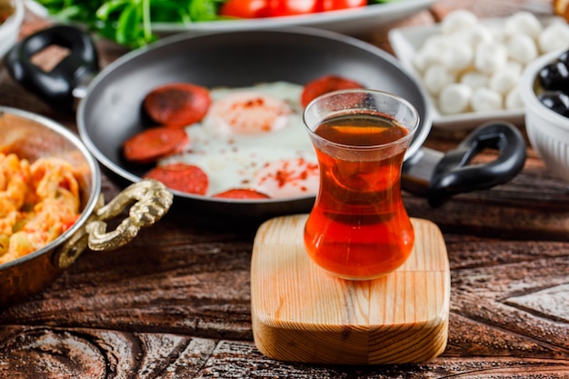 Free photo side view a cup of tea with delicious meals on wooden surface