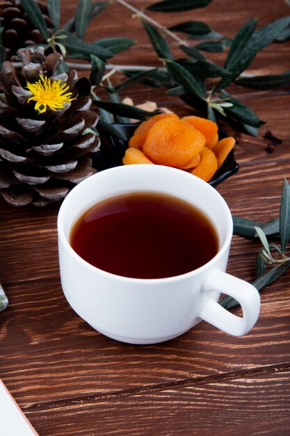 Side view of a cup of tea with dried apricots on wood