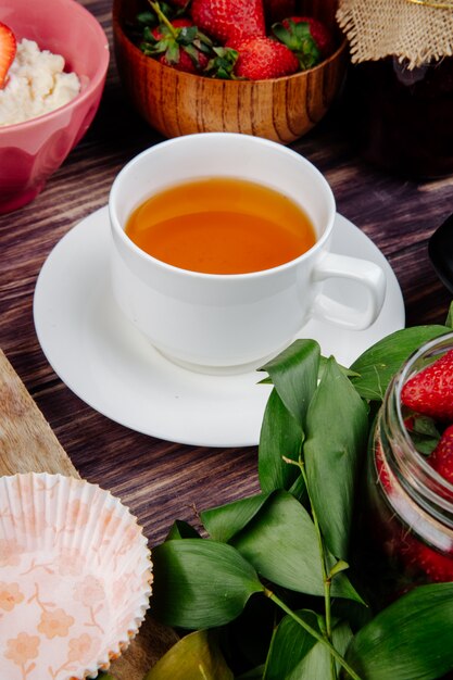 Side view of a cup of tea with fresh ripe strawberries on rustic