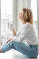 Free photo side view of curly-haired blonde woman relaxing at home with a coffee cup