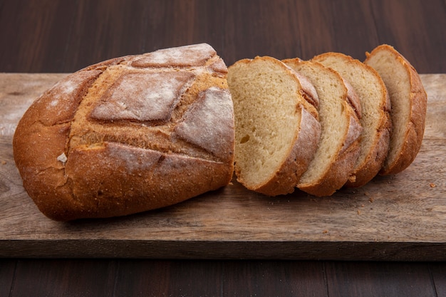 Side view of cut and sliced crusty bread on cutting board on wooden background