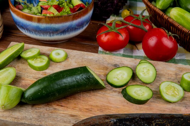 Side view of cut and sliced cucumber on cutting board with tomatoes vegetable salad on wooden table