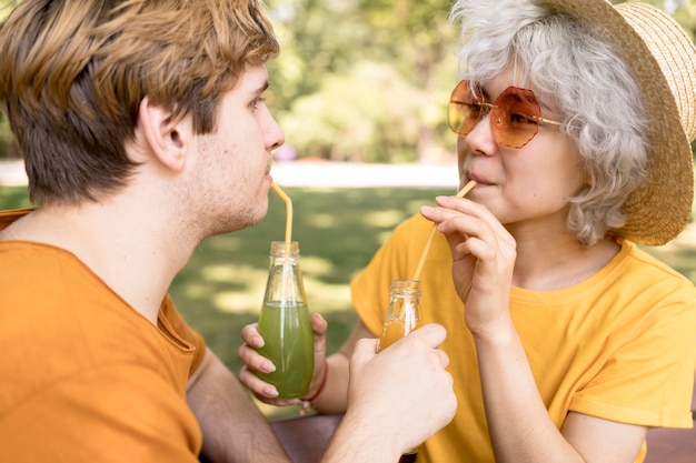 Side view of cute couple drinking juice in the park with straws