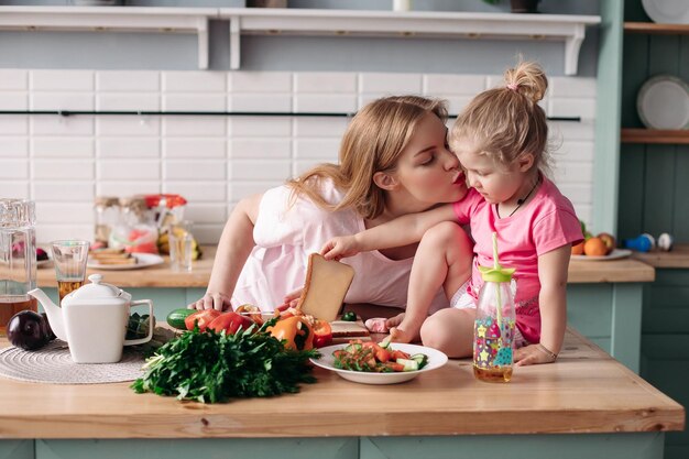 Side view of cute mother and daughter hugging and kissing each other in morning Family sitting at kitchen cooking breakfast and cutting vegetables at home Concept of lunch and food