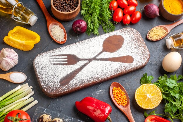 Side view of cutting board with flour drawn fork knife among fresh vegetables different spices green bundles