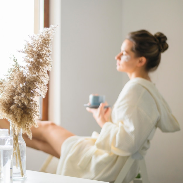 Free photo side view of defocused woman enjoying a spa day at home while having coffee