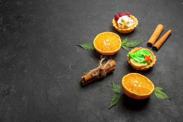 Side view of delicious cookies cinnamon limes and half cut oranges with leaves on dark background