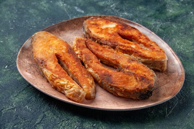 Side view of delicious fried fish on a brown plate on the left side on mix colors table with free space