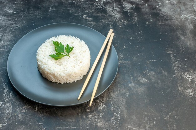 Side view of delicious rice meal served with green and chopsticks on a black plate on the right side on dark background