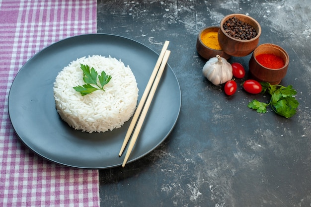 Free Photo side view of delicious rice meal served with green wooden chopstics on a black plate on purple stripped towel and different spices garlic tomatoes on dark background