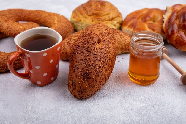 Side view of delicious sesame patties with a cup of tea and honey on a glass jar and different buns isolated on a white background